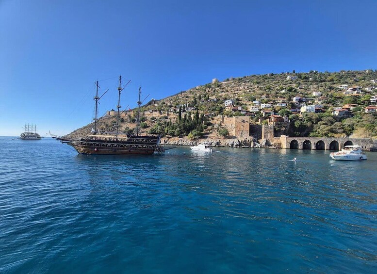 A coastal town with a historic fort, a large sailing ship, and a smaller boat in the water. 2