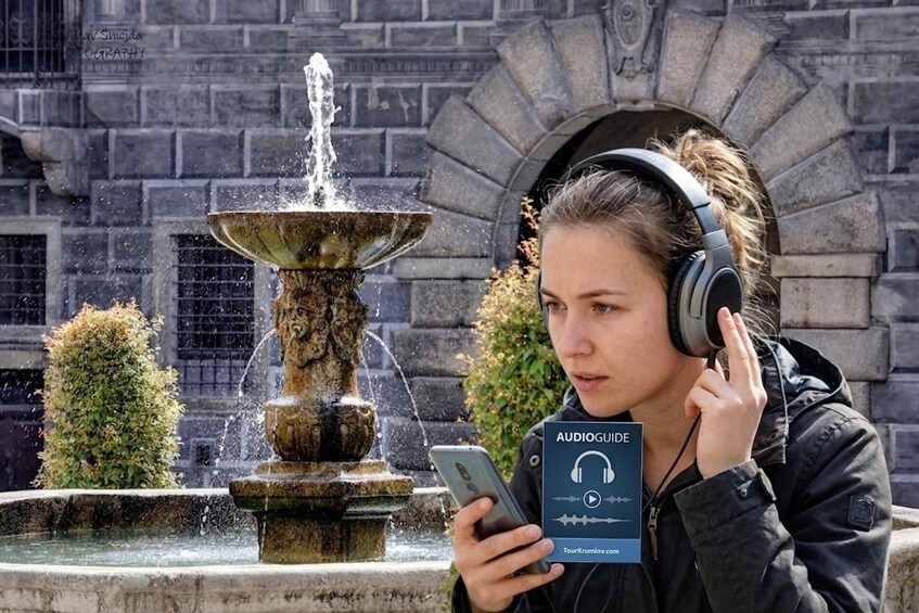 A person with headphones and a smartphone, standing in front of a stone fountain. 2