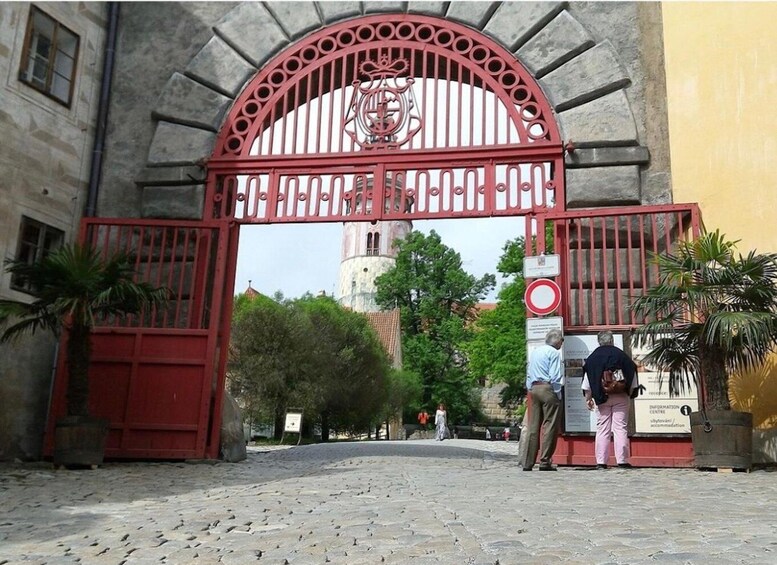 A red gate with a coat of arms, leading to a building with a clock tower. 3