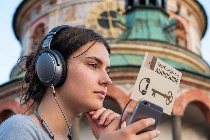 A person wearing headphones and holding a smartphone with an audioguide. 1