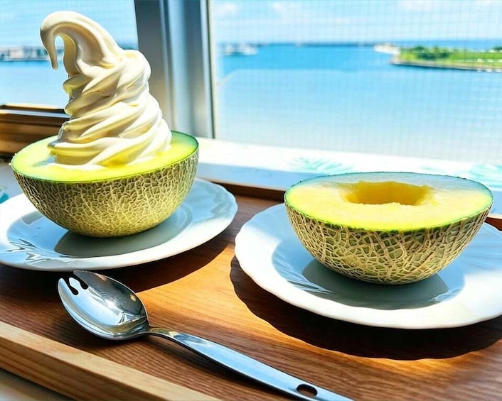 Two bowls of melon soup and a spoon on a wooden table by a window overlooking a body of water. 3