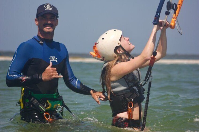 A person in a wetsuit and a helmet, holding a kiteboard, with another person assisting. 5