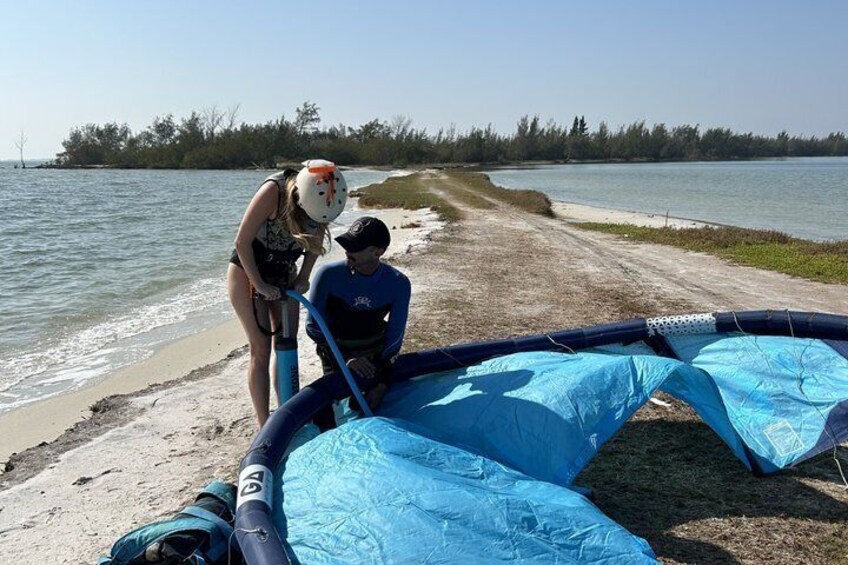 A beach with a deflated blue inflatable raft and a person inflating it. 4