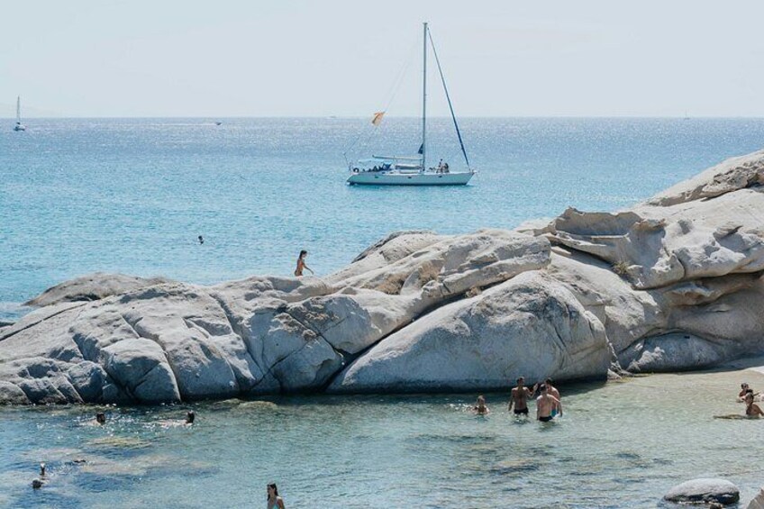 A rocky shoreline with people swimming and a sailboat in the distance. 5