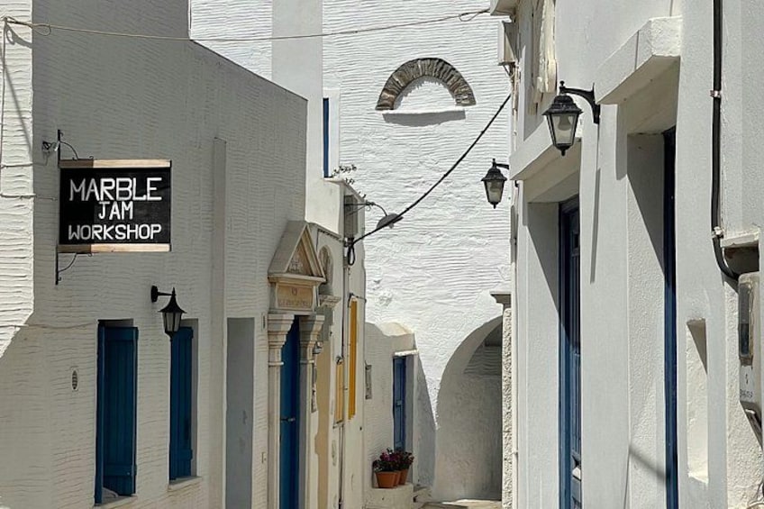 A narrow street with white buildings, a sign for 'MARBLE JAM WORKSHOP,' and blue shutters. 2