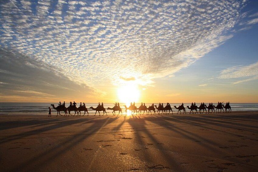A sunset over a beach with silhouettes of people riding camels. 3