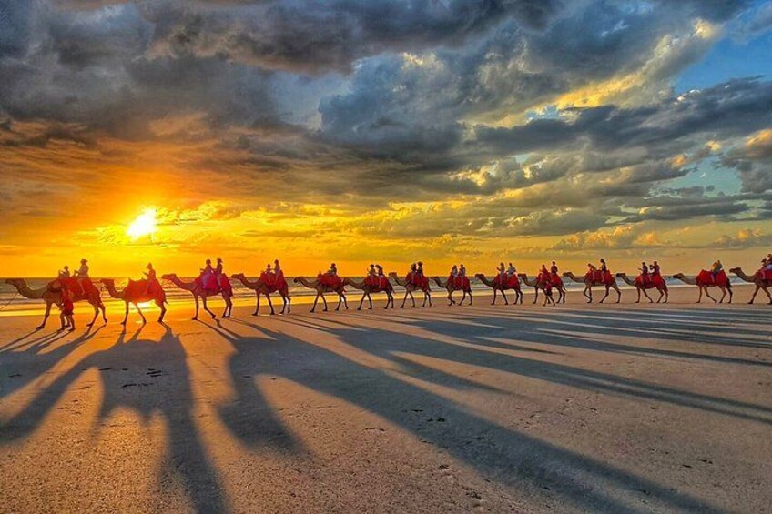 A group of people riding camels on a beach at sunset. 2