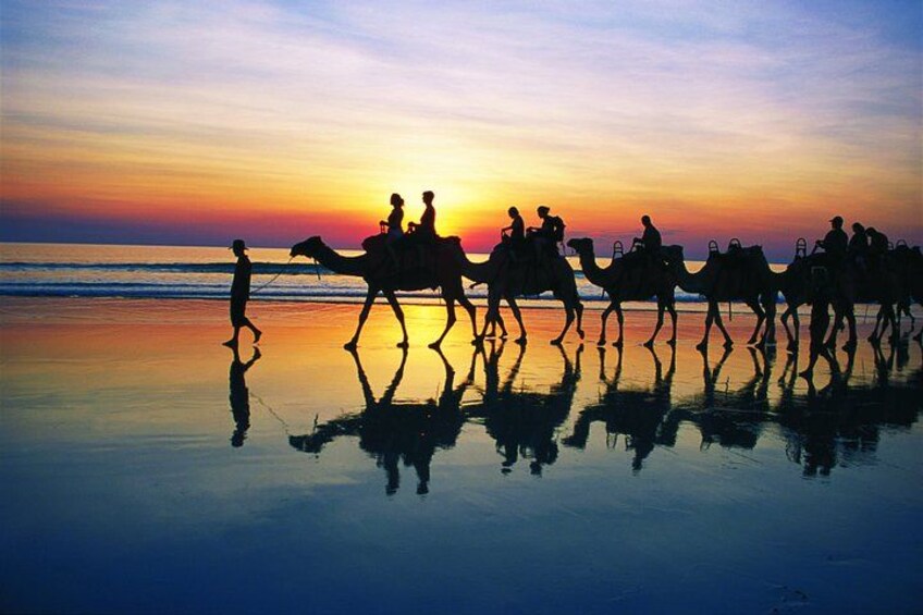 A sunset over a beach with people riding camels. 5
