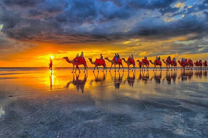 A sunset over a reflective water surface with camels and riders. 1