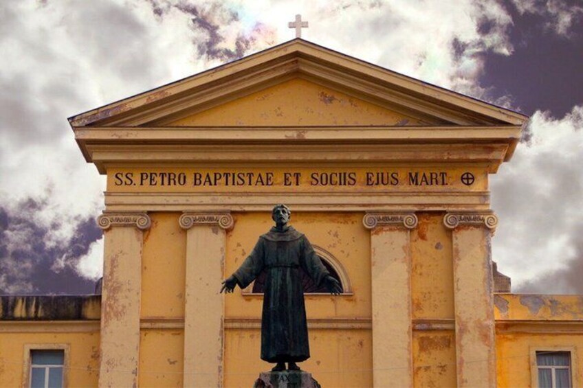 En byggnad med en staty och en inskription som lyder: ”SS. PETRO BAPTISTAE ET SOCHIS EJUS MART.” 2