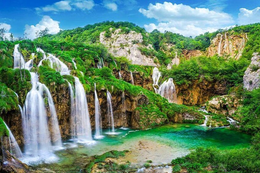 A waterfall cascading into a turquoise pool surrounded by lush greenery and rocky cliffs. 1