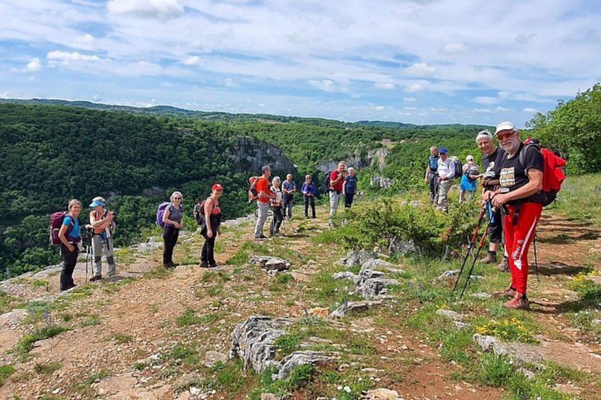 A group of hikers on a mountain trail with rocky terrain and lush greenery in the background. 2