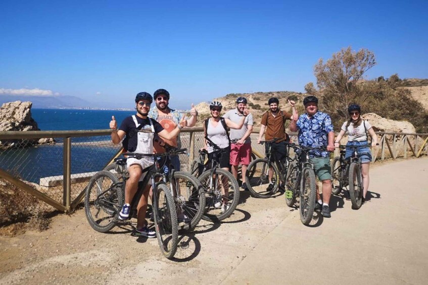 A group of cyclists on a coastal path with a view of the sea and distant mountains. 4