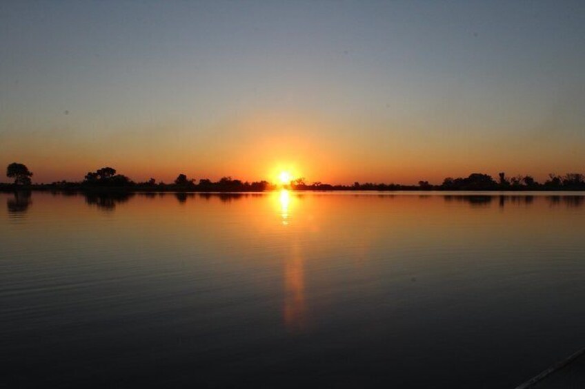 A sunset over a calm lake with silhouettes of trees and a distant shoreline. 3