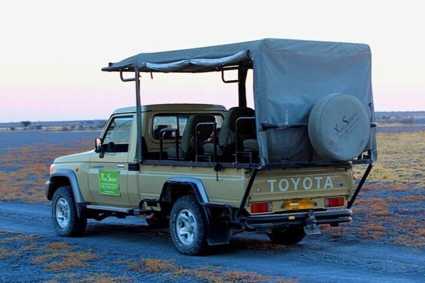 A Toyota off-road vehicle with a canvas top and spare tire on the back, parked on a dirt road. 3