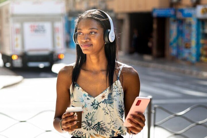 Une personne tenant un téléphone intelligent et une tasse, portant des écouteurs et se tenant sur un trottoir. 1