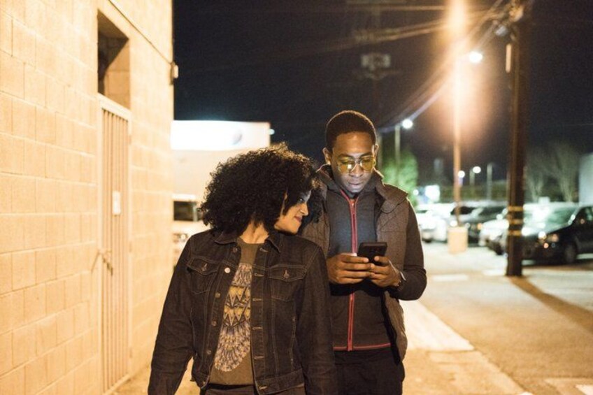 Dos personas de pie en una acera de noche, una sosteniendo un teléfono inteligente. 4