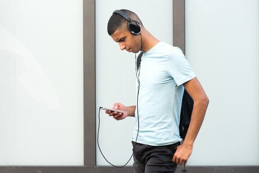 Une personne portant un casque audio, tenant un téléphone intelligent et appuyée contre un mur. 2