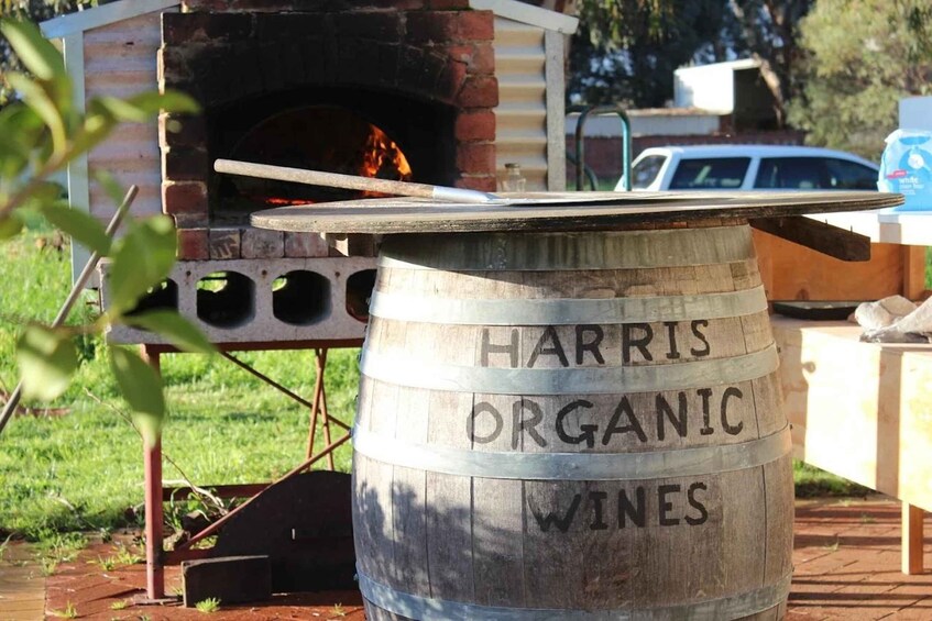 A wooden barrel labeled 'HARRIS ORGANIC WINES' with a brick oven in the background. 1