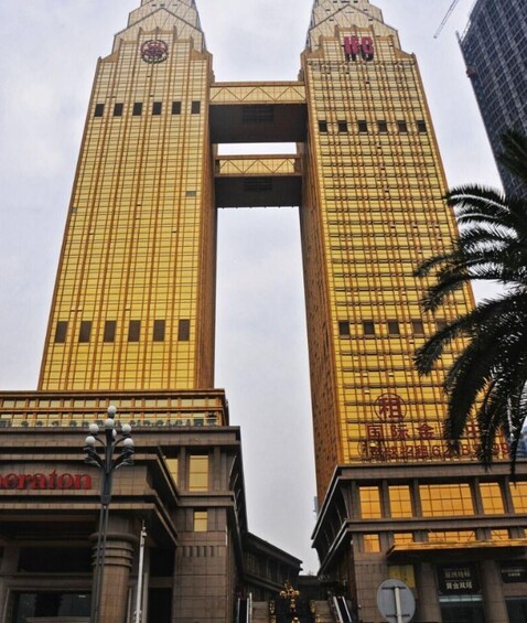 A tall, yellow building with a distinctive archway connecting two towers, and a palm tree in the foreground. 1