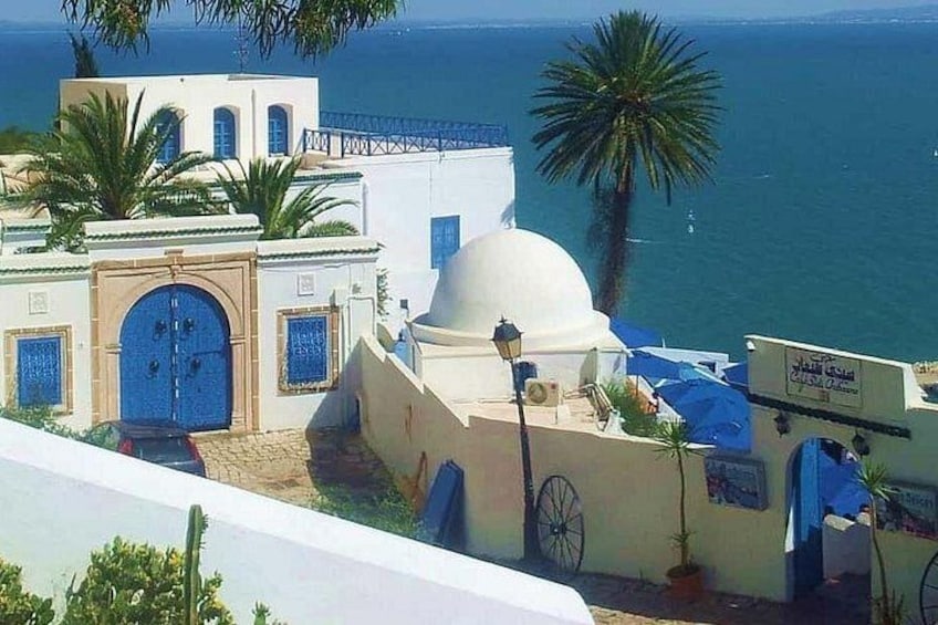 A coastal building with blue doors and a dome, palm trees, and a view of the sea. 3