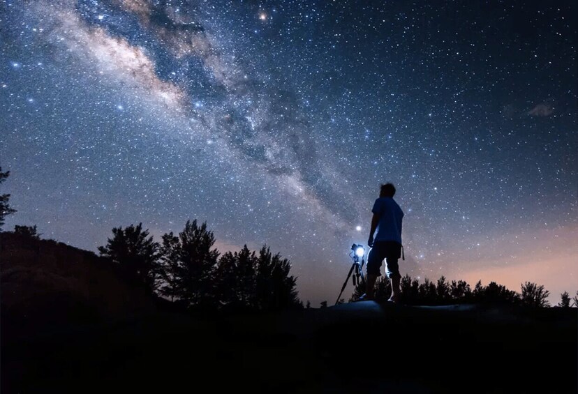 A person standing on a hill under a starry night sky with a telescope. 4