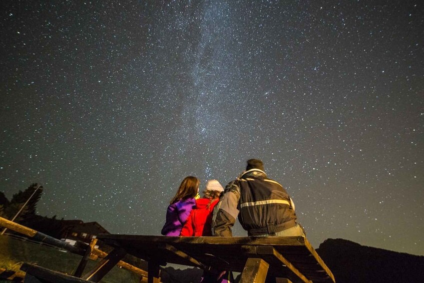 Three people observing the night sky from a wooden platform. 5