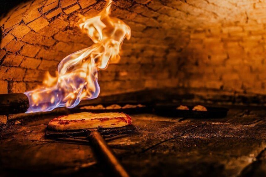 Une pizza cuite dans un four en briques, avec des flammes. 1