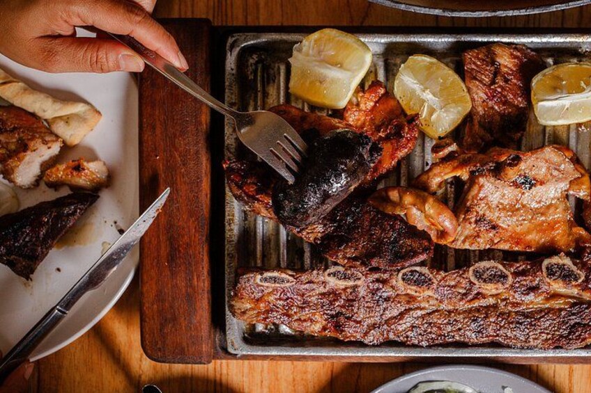 A variety of grilled meats on a tray, including ribs and chicken, with lemon wedges on the side. 3