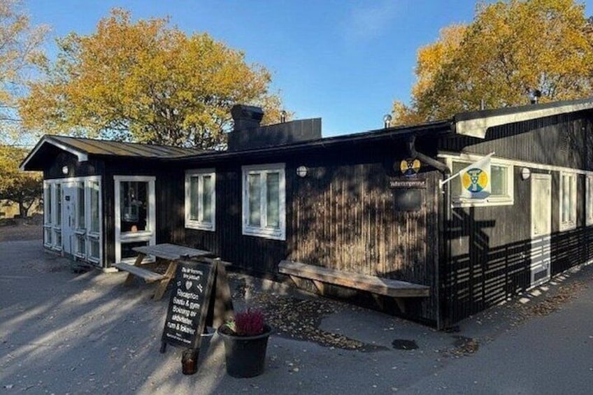 A rustic wooden building with a signboard, benches, and a potted plant. 3