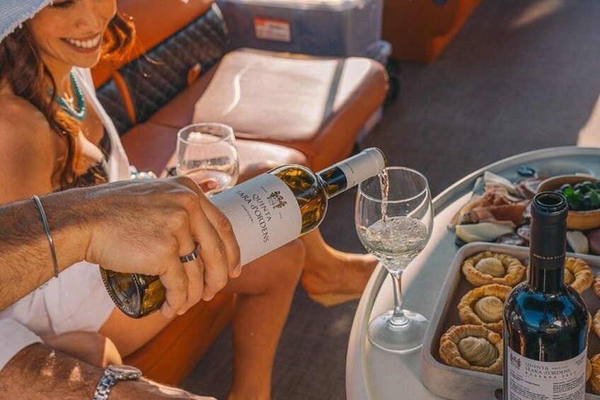 A person pouring wine into a glass, a bottle of wine, and a tray with food and drinks. 5