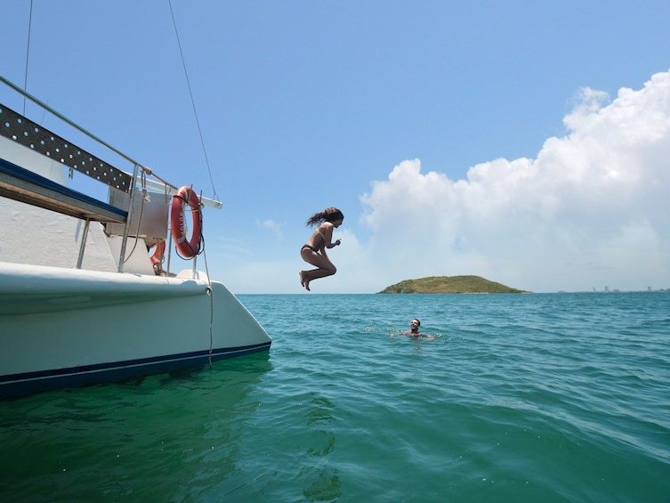A person jumping from a boat into the water, another person swimming, and a distant island. 1