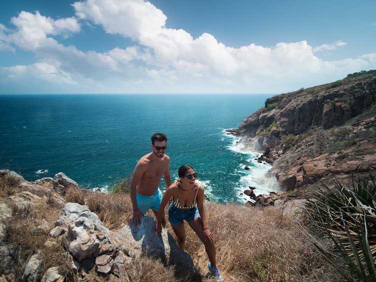 A couple standing on a rocky cliff overlooking a coastal view with the ocean and a clear sky. 5