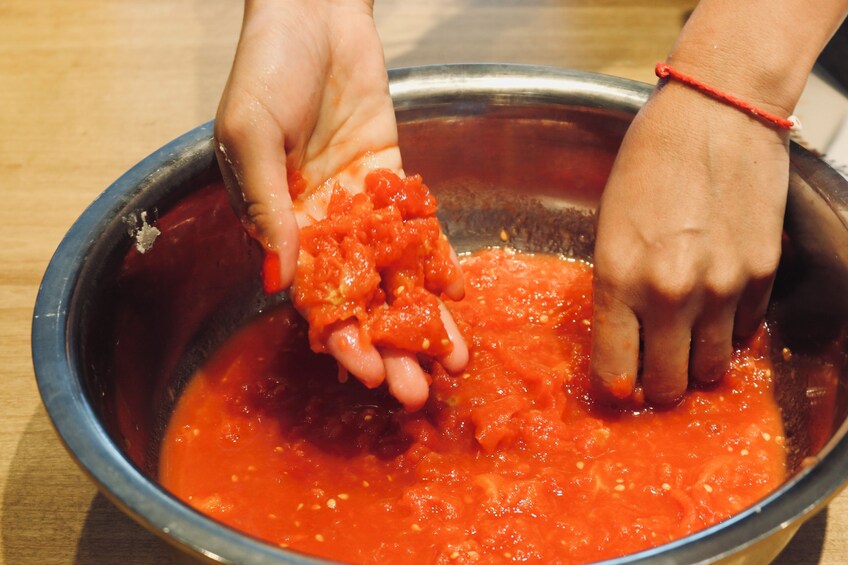 Hands mixing a red sauce in a metal bowl. 4