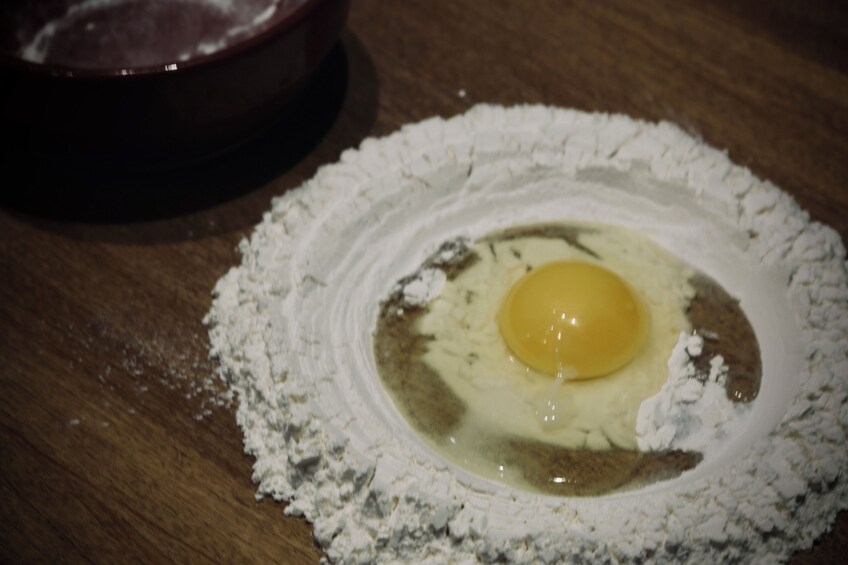 A bowl with flour and a raw egg yolk in the center. 3