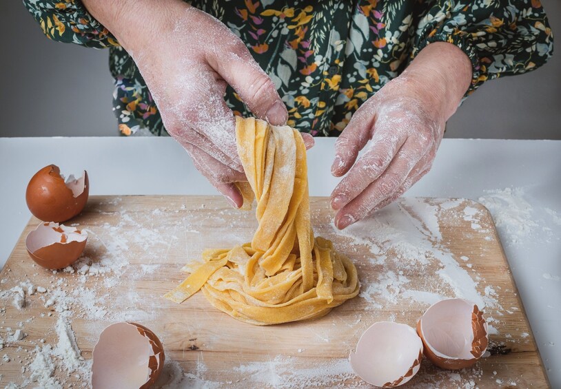 Hands shaping pasta dough on a wooden surface with flour scattered around. 1
