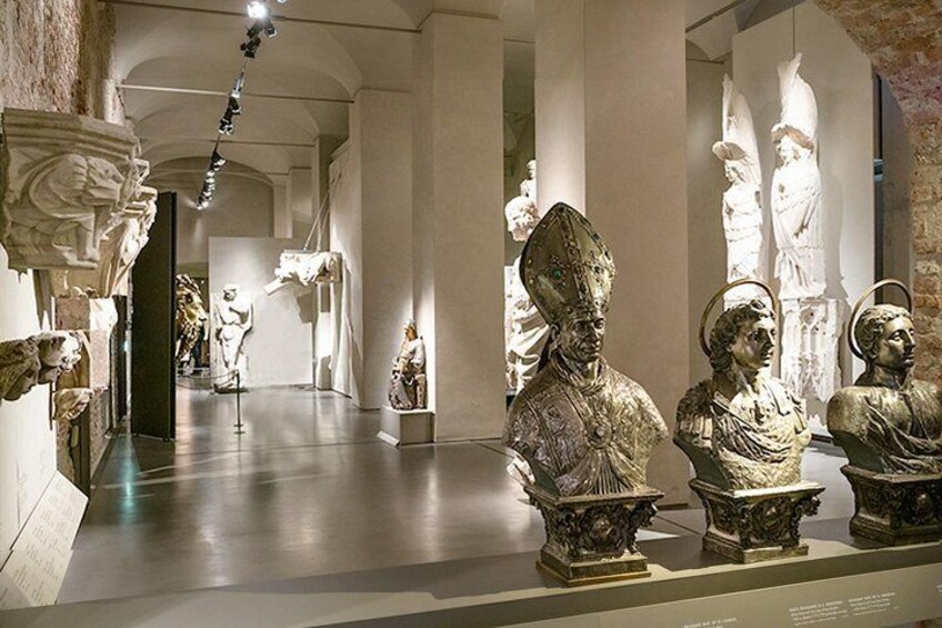 En museikorridor med klassiska skulpturer och byster placerade på piedestaler. 2