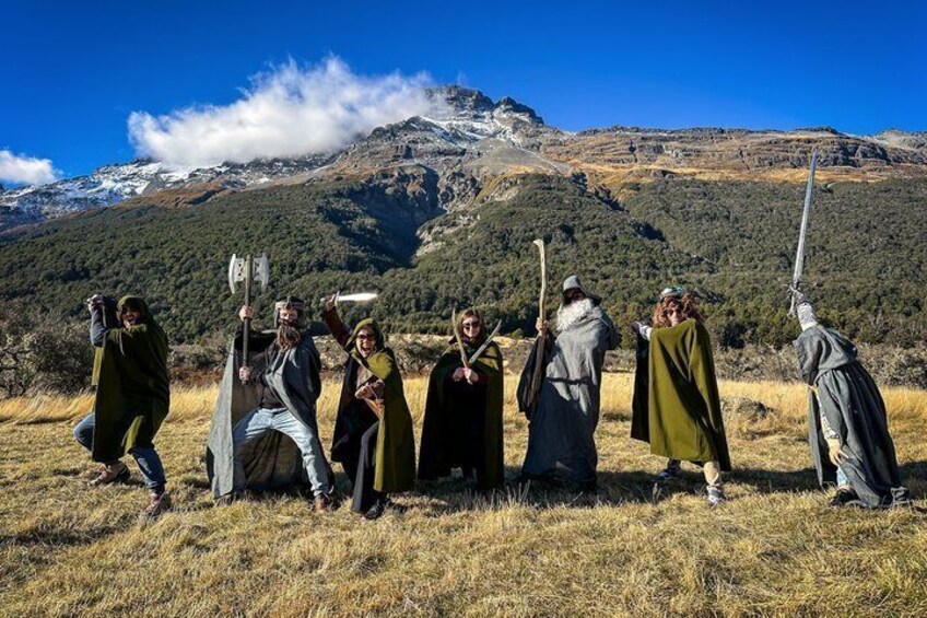 Un grupo de personas vestidas con trajes medievales, con espadas y escudos, en un campo cubierto de hierba con montañas al fondo. 3