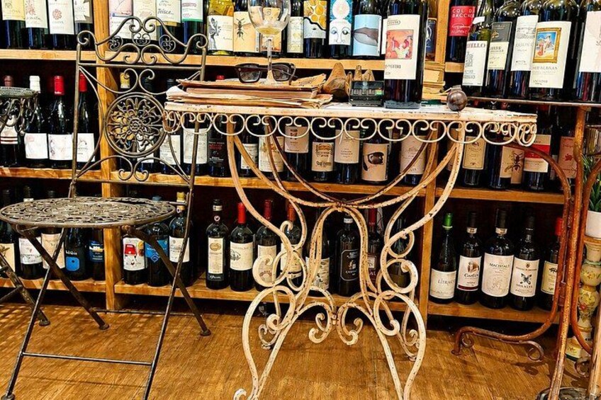 A wine shop with a metal table and chairs, shelves of wine bottles, and a wooden floor. 5