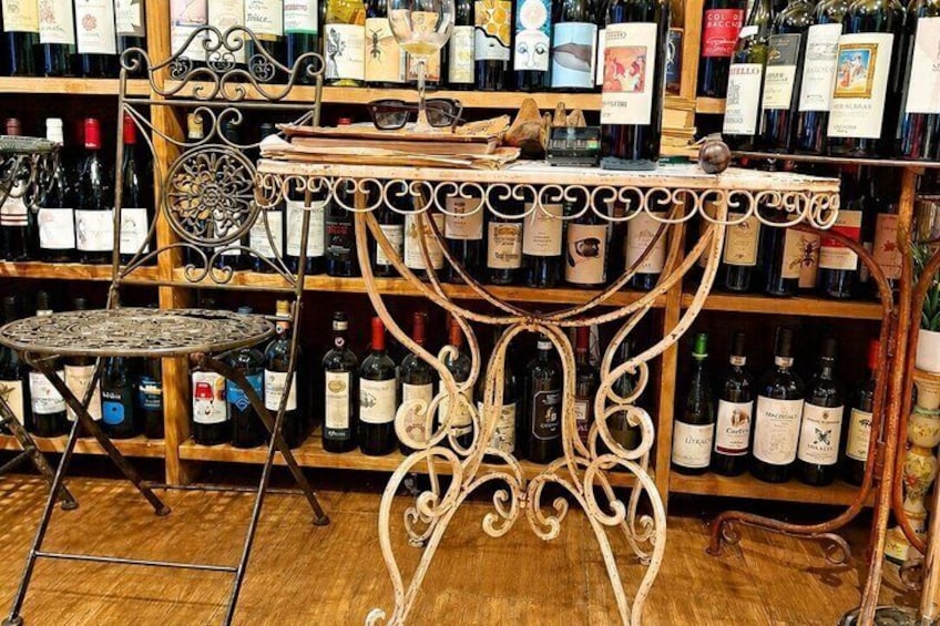 Un negozio di vini con un tavolo e sedie in ferro battuto, scaffali pieni di bottiglie e un pavimento in legno. 5