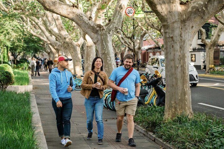 Un marciapiede alberato con pedoni, biciclette parcheggiate e un segnale di limite di velocità. 1