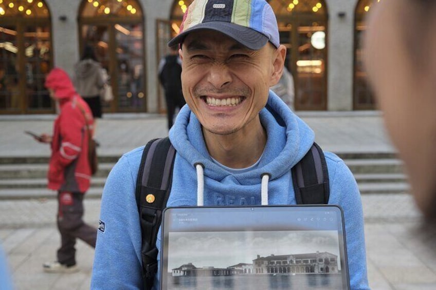 Una persona che tiene in mano un tablet con un'immagine di un edificio, indossa una felpa blu e un berretto, e porta uno zaino. 3