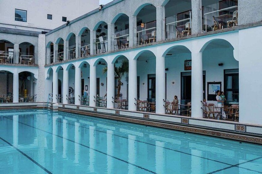 En swimmingpool med en hvid bygning, der har buede balkoner og udendørs siddepladser. 3