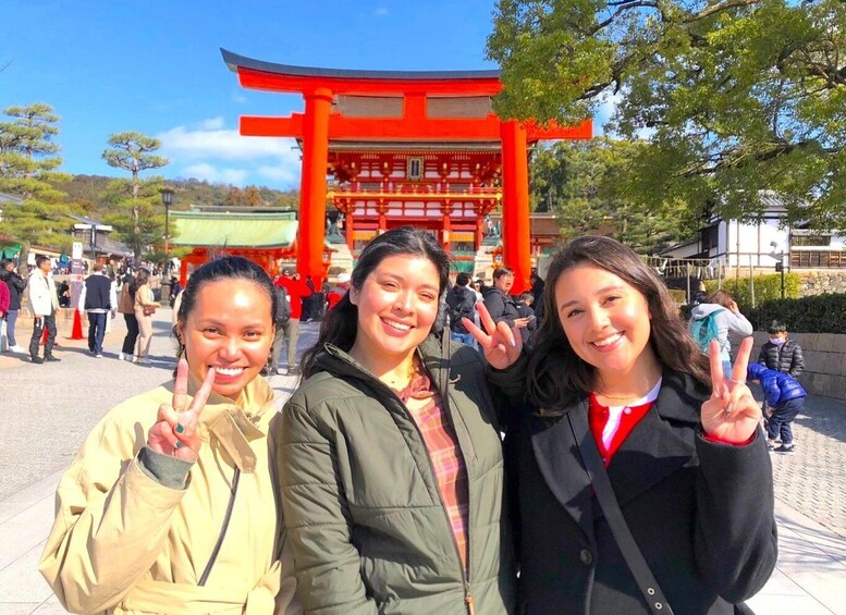 Three people posing in front of a red torii gate with a traditional Japanese building in the background. 1