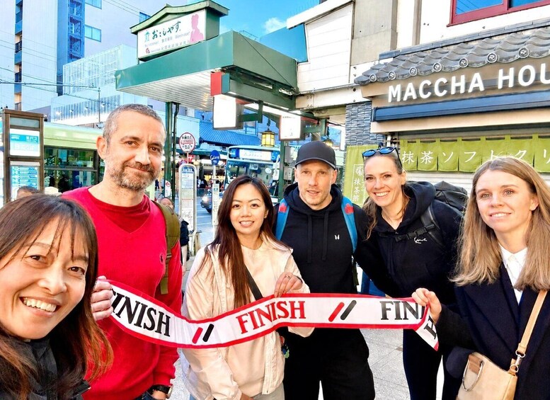 A group of people holding a finish ribbon, standing in front of a building with a sign that reads 'MACCHA HOUSE'. 3