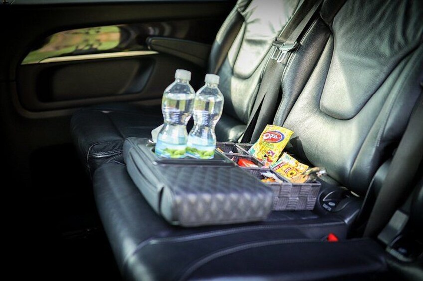 A car's back seat with a folded blanket, two water bottles, a snack pack, and a small box. 4