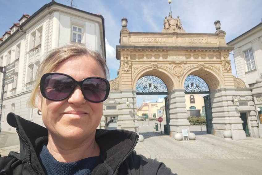 Eine Frau vor einem historischen Bogenwerk mit aufwendigen Verzierungen und einer Statue darauf. 1