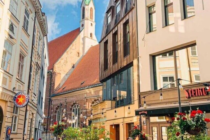 A street with historic buildings, a church tower, and a shop with a red sign. 3