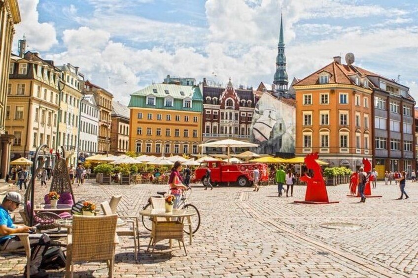 A cobblestone square with outdoor seating, a red bus, and historic buildings. 2