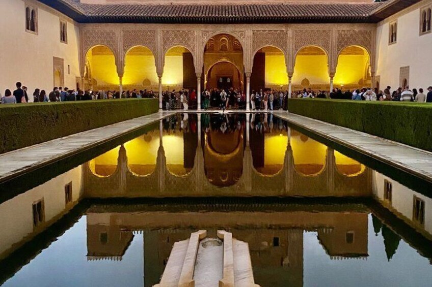 A courtyard with a reflective pool, arches, and people gathered around. 1